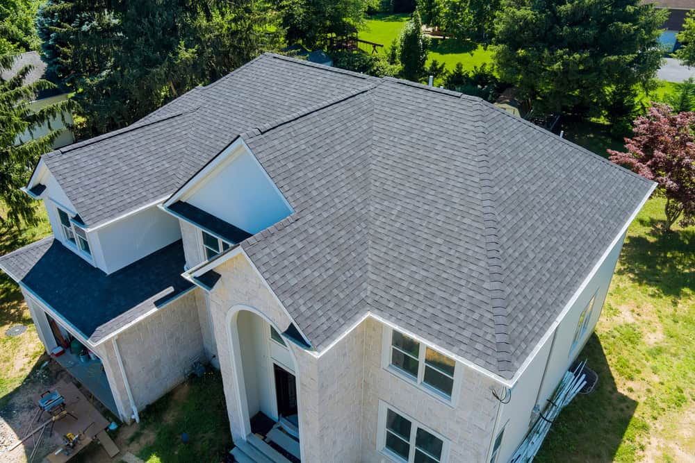 Aerial view of a large two-story house with a dark gray shingled roof. Nestled amidst green trees, the property boasts a well-maintained lawn. The architecture features a prominent arched entryway and multiple gables, showcasing the precision often admired by Land Surveyors in Indian River County.