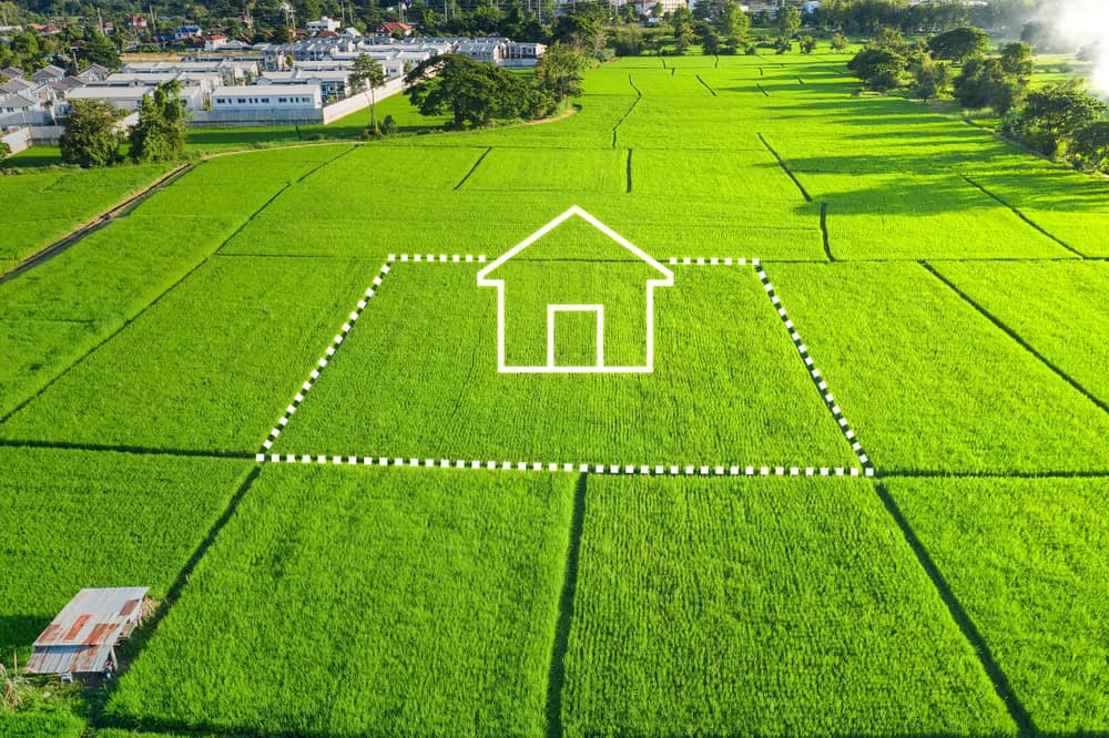 A large, vibrant green rice field with an outlined shape of a house in the center, indicating a planned building site. A small shed is visible at the bottom, and there are buildings and trees in the distance—a testament to Land Surveyors Martin County's precision.