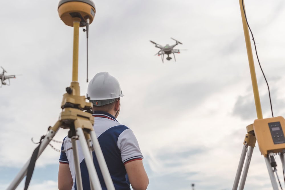A person in a white hard hat operates a drone outdoors, surrounded by surveying equipment under a cloudy sky. This professional exemplifies the expertise of Land Surveyors in Martin County.