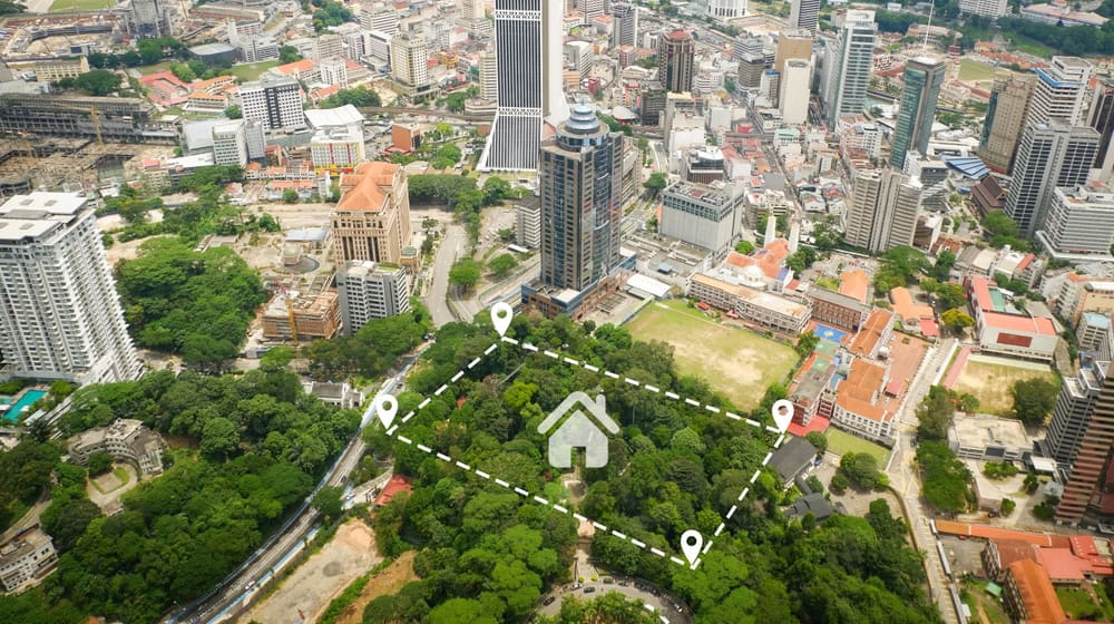 Aerial view of a city with tall buildings, roads, and greenery. A section of land is highlighted with a dashed line and location markers, overlaid with a house icon, suggesting an area of interest or property for development by Land Surveyors in Martin County.