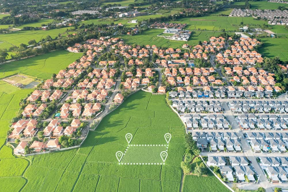 Aerial view showing a sprawling residential area surrounded by lush green fields, with orange-tiled roofs forming a distinct shape. Some marked locations feature white pins and lines, possibly highlighted by land surveyors in Martin County.